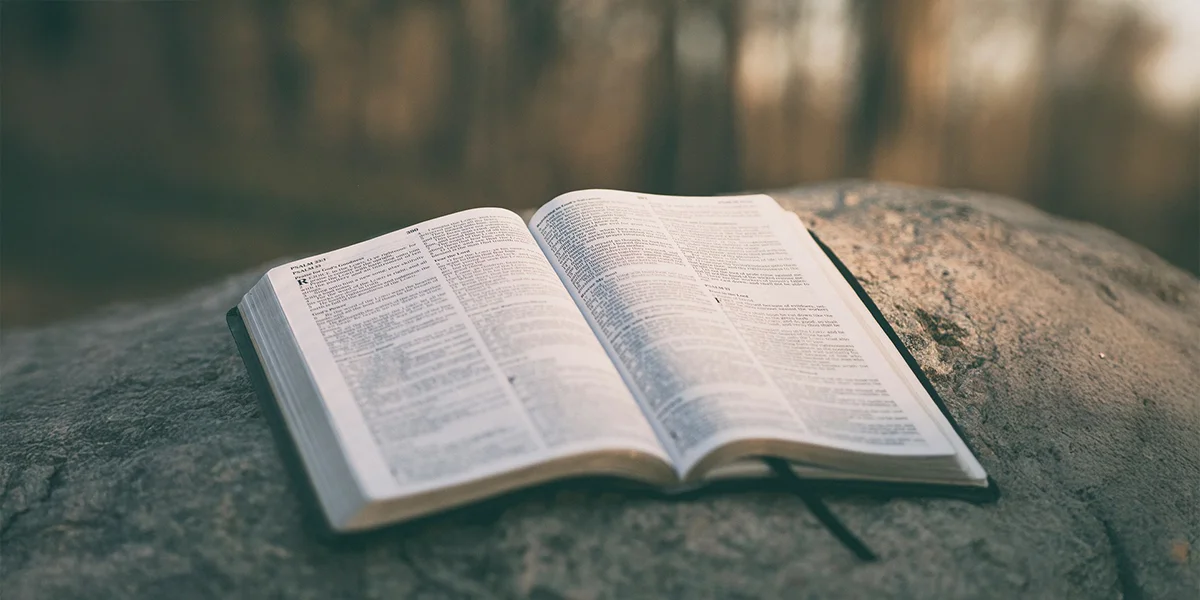 Image of an open bible on a bolder with reflection on water in the background